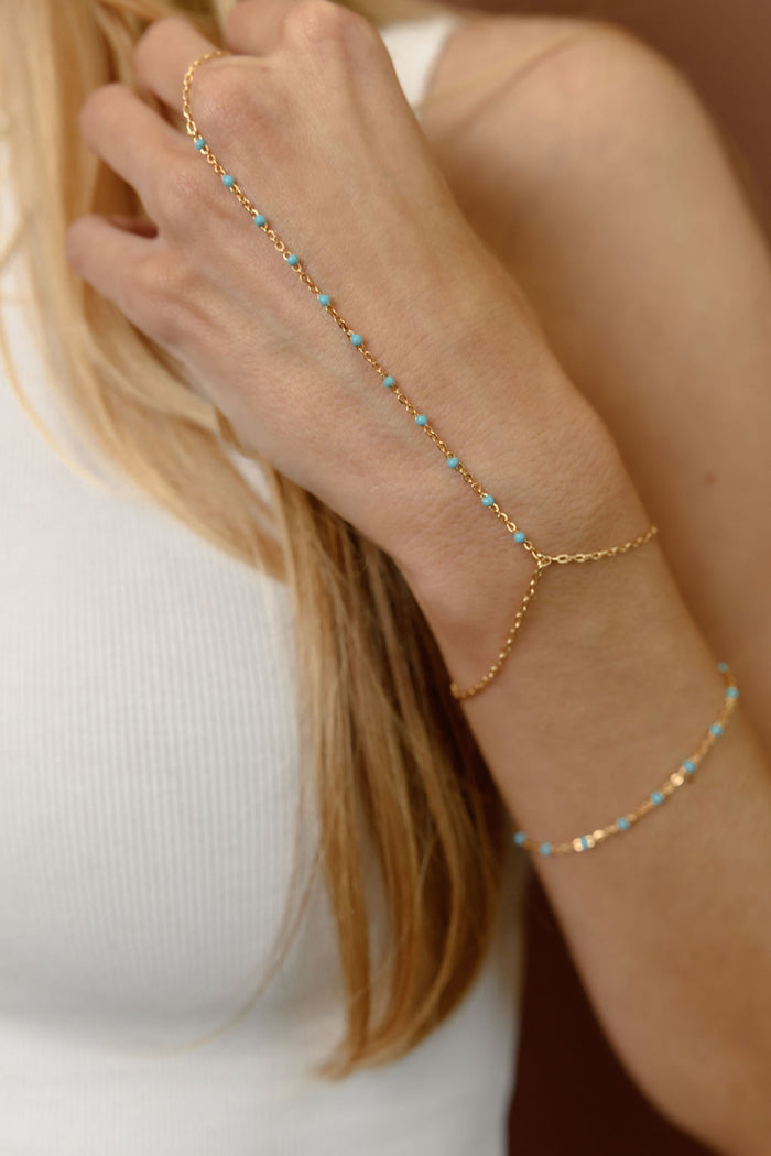 Close up of a wrist with gold and teal bracelets