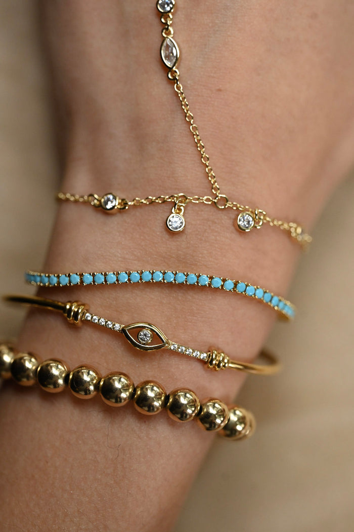 Close-up of a wrist wearing multiple gold and turquoise bracelets on a neutral background