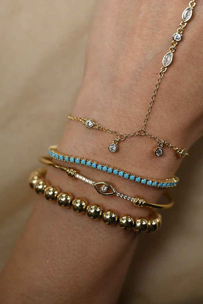 Close-up of a wrist wearing multiple gold and turquoise bracelets on a beige background