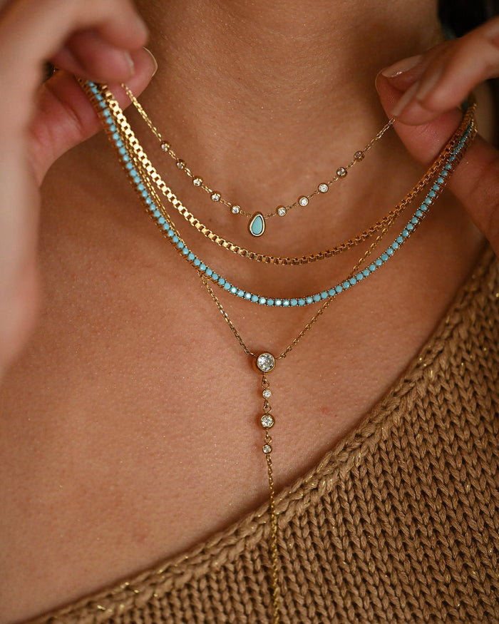 Close-up of a person wearing multiple gold and turquoise necklaces.