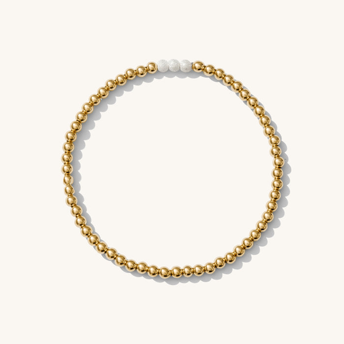 Close up of a gold bead bracelet with silver accent beads on a white background