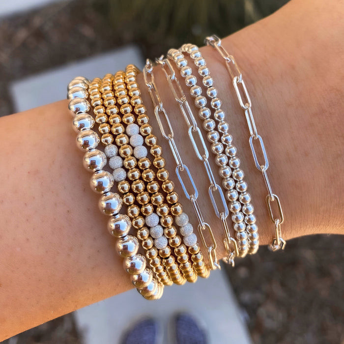 Close up of a wrist with gold bead & gold link bracelets on a brown background