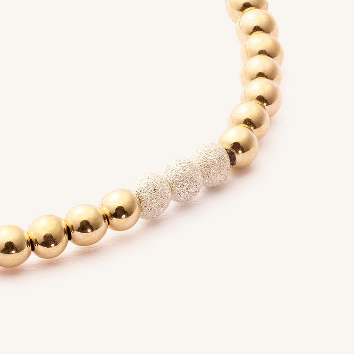 Close up of a gold bead bracelet with silver accent beads on a white background