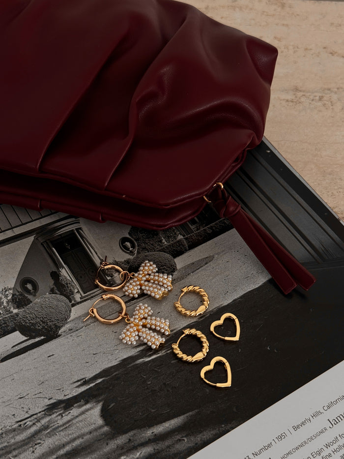 Three pairs of statement hoop earrings on a magazine background with a red purse