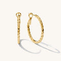 Close up of textured gold earrings on a white background