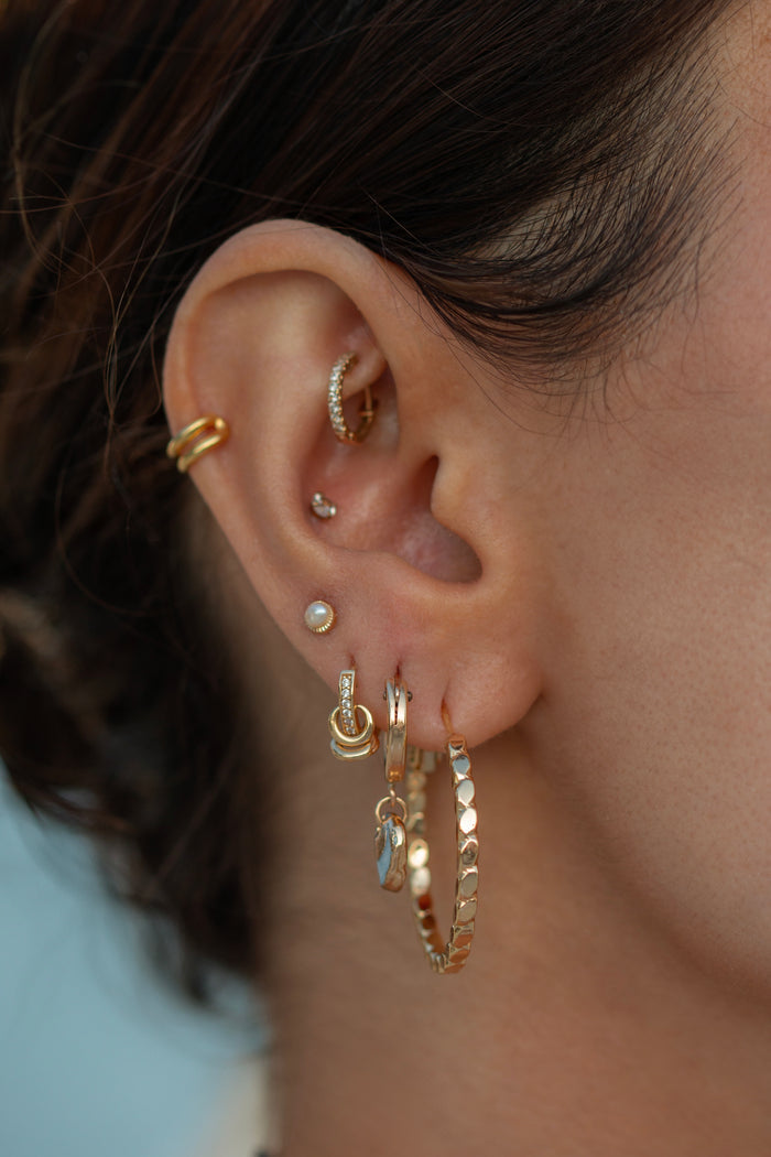 Close-up of an ear with multiple gold and crystal earrings