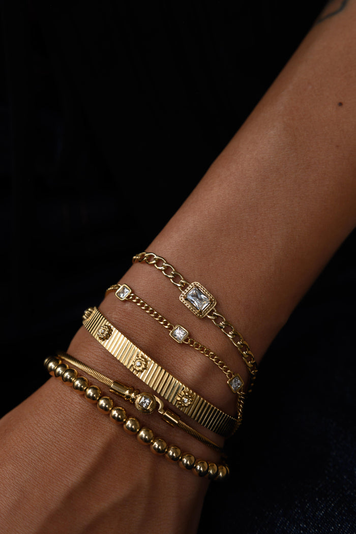 A wrist with gold bracelets on a black background