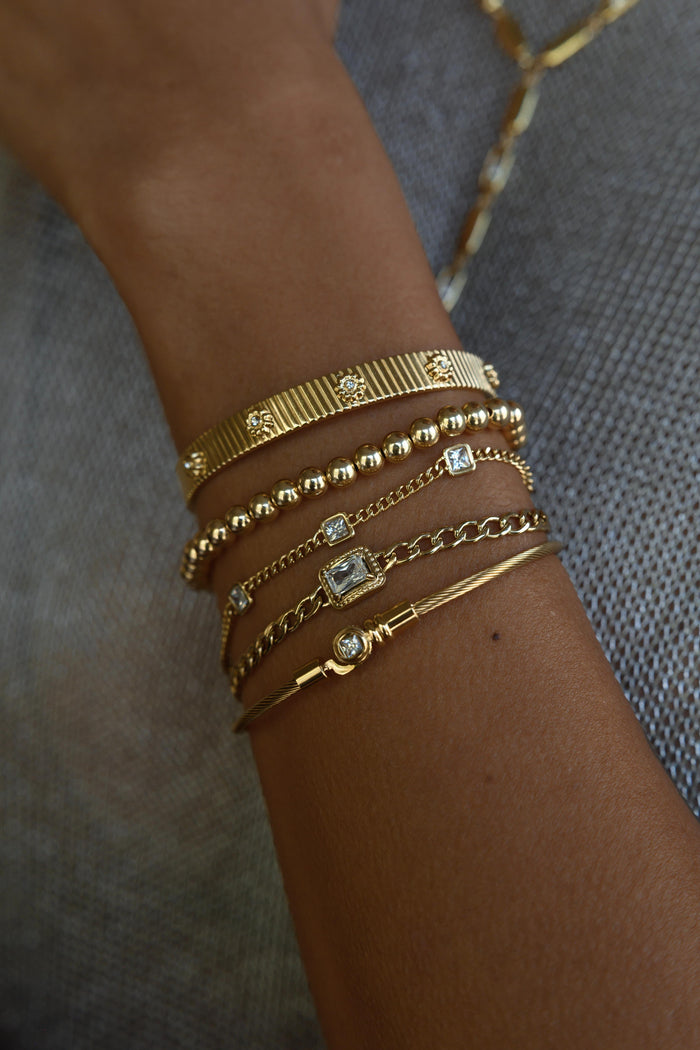 Close up of a wrist with gold bracelets on a grey background