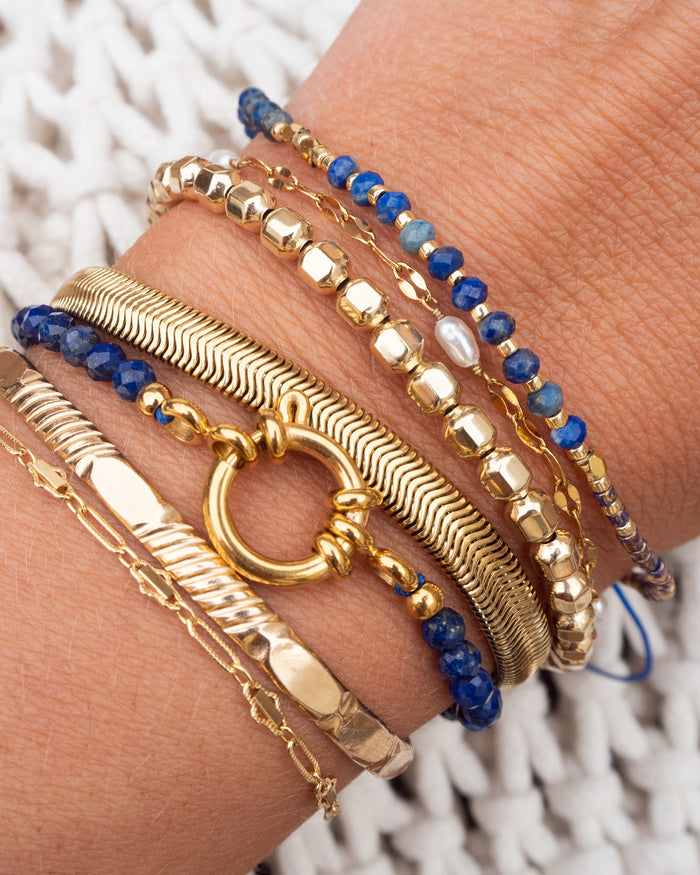 Close up of a wrist with blue and gold bracelets on a white background