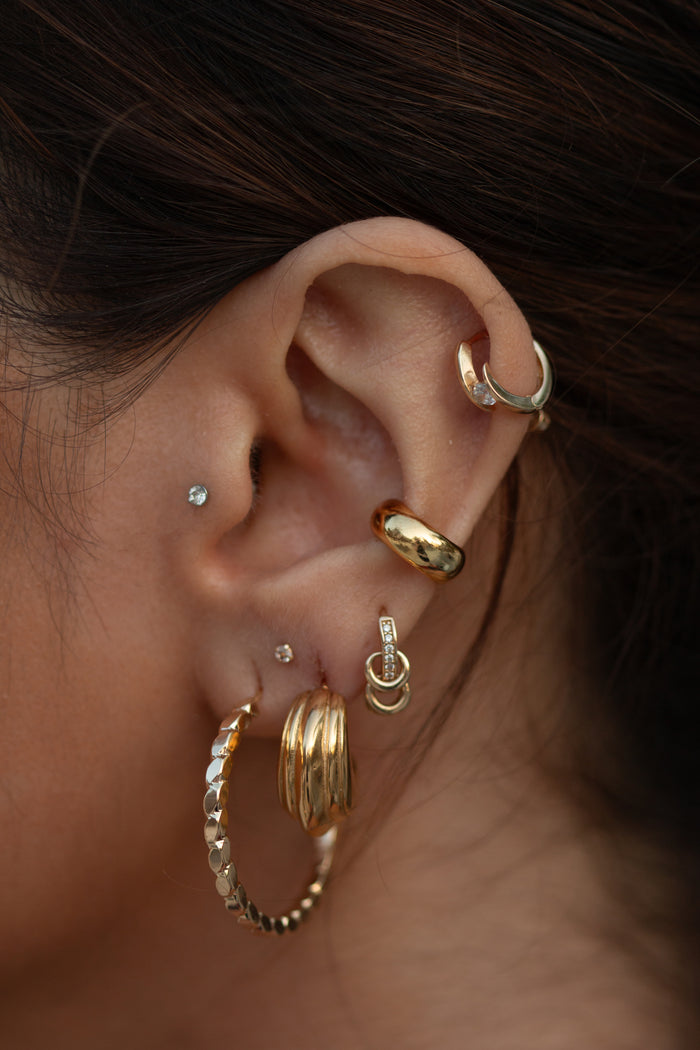 Close-up of an ear with multiple gold and crystal earrings