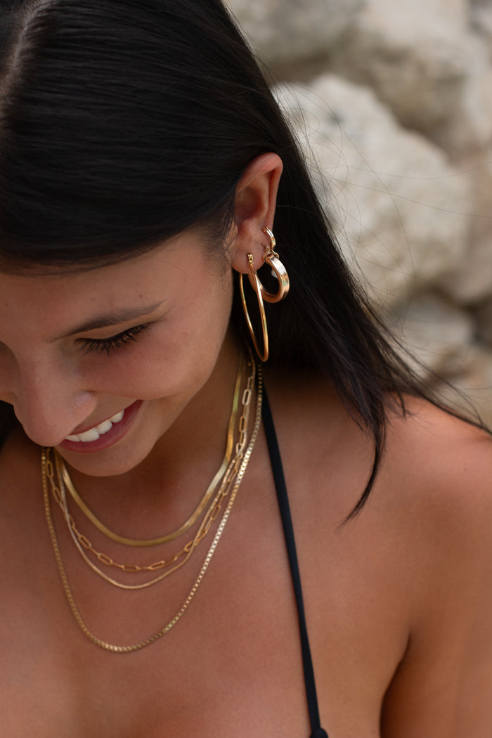 A woman wearing layered gold earrings and necklaces