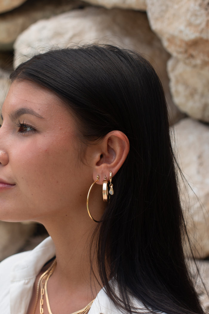 Side profile of a woman wearing multiple gold hoop earrings and necklaces