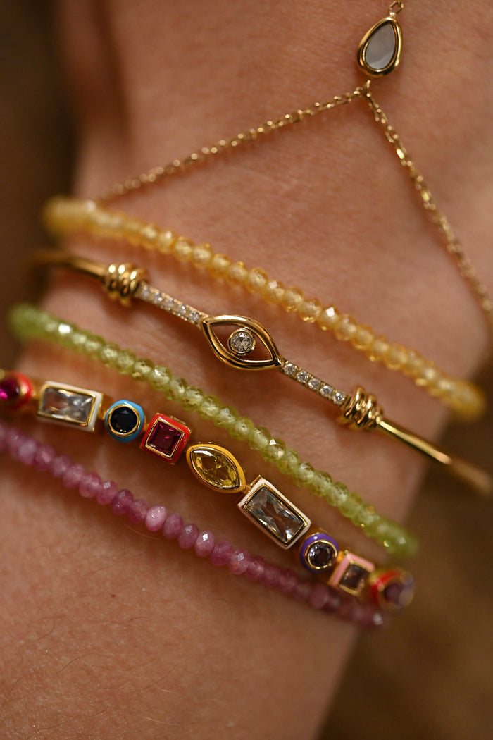 Close-up of a wrist wearing multiple gold and gemstone bracelets.