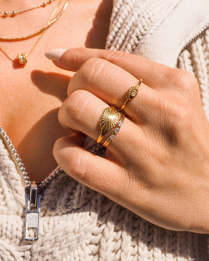 Close up of a hand wearing the dainty Yaz eye ring alongside slim gold bands